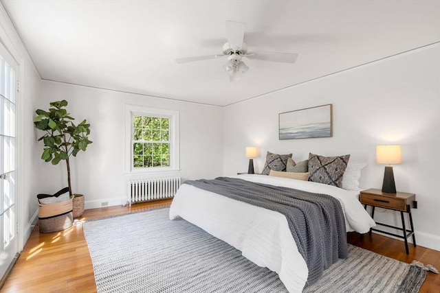 bedroom with radiator, baseboards, wood finished floors, and a ceiling fan