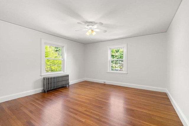 unfurnished room with radiator, healthy amount of natural light, ceiling fan, and wood finished floors