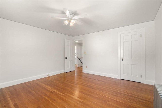 empty room featuring radiator, light wood-style flooring, baseboards, and a ceiling fan