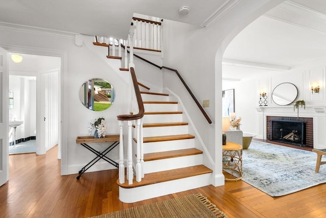 stairs featuring hardwood / wood-style floors, arched walkways, a brick fireplace, baseboards, and beam ceiling