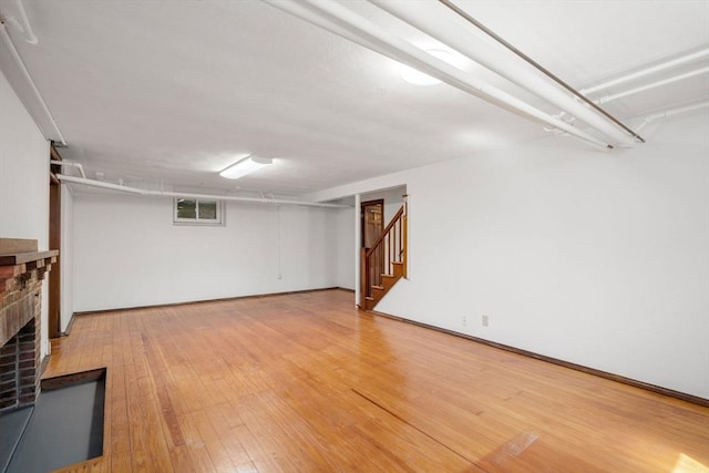 finished basement featuring light wood-type flooring, stairs, and a brick fireplace