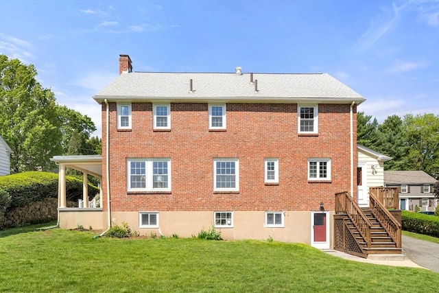 back of house featuring a chimney, a yard, brick siding, and stairs