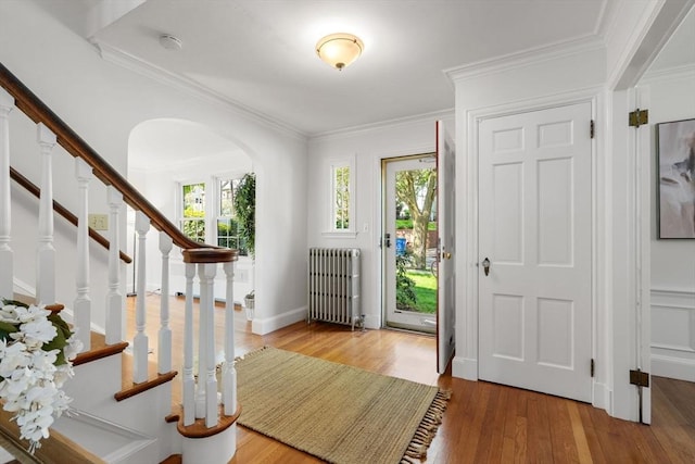entrance foyer featuring radiator heating unit, arched walkways, wood finished floors, ornamental molding, and stairway