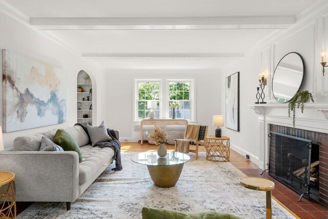 living area featuring beamed ceiling, a brick fireplace, baseboards, wood finished floors, and crown molding