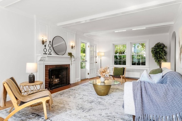 living area featuring a fireplace, wood finished floors, beamed ceiling, arched walkways, and ornamental molding