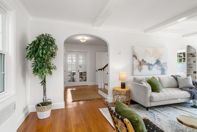living area featuring arched walkways, wood finished floors, beamed ceiling, baseboards, and ornamental molding