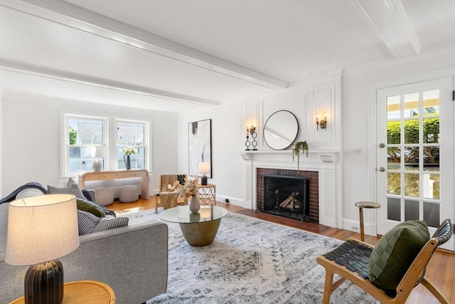 living area featuring beamed ceiling, a fireplace, wood finished floors, and baseboards