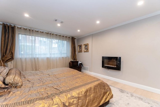 bedroom featuring visible vents, crown molding, baseboards, wood finished floors, and a glass covered fireplace