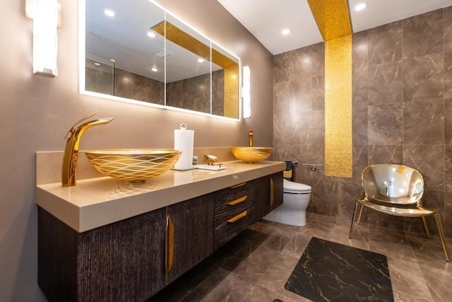 full bath with tile walls, toilet, double vanity, and a sink