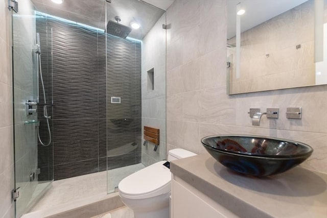 bathroom with vanity, tile walls, toilet, and a shower stall