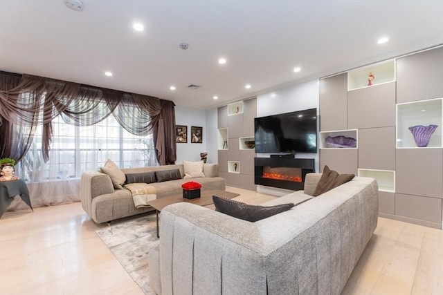 living area with a glass covered fireplace, recessed lighting, light wood-style floors, and visible vents