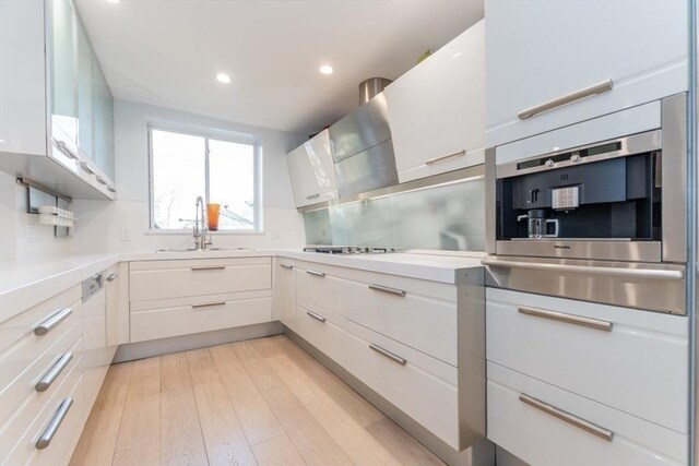 kitchen featuring light wood finished floors, a sink, wall oven, white cabinets, and light countertops