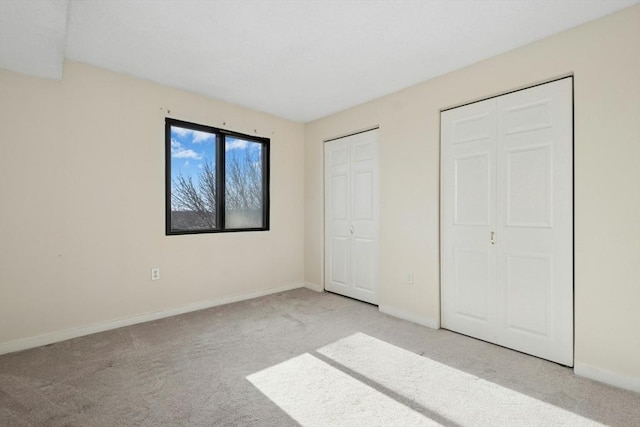 unfurnished bedroom with carpet floors, baseboards, and multiple closets