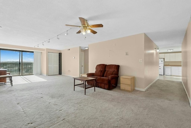 living area with carpet, rail lighting, a ceiling fan, and baseboards