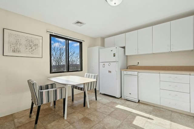 kitchen featuring visible vents, light countertops, freestanding refrigerator, and white cabinets