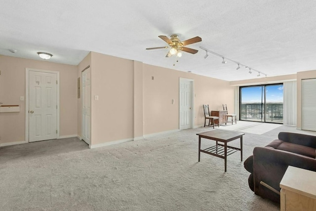 carpeted living area with rail lighting, ceiling fan, baseboards, and a textured ceiling