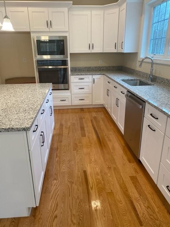 kitchen featuring pendant lighting, sink, white cabinetry, light wood-type flooring, and stainless steel appliances