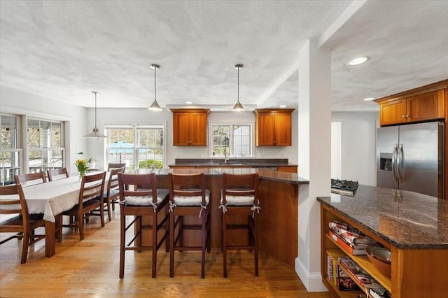 76 Union St, Natick, MA 01760 - kitchen with brown cabinetry, light wood-type flooring, a textured ceiling, stainless steel fridge with ice dispenser, and a sink