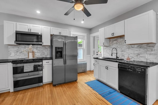 kitchen with appliances with stainless steel finishes, radiator heating unit, a sink, dark countertops, and recessed lighting