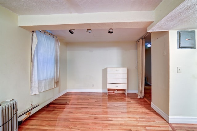 unfurnished room featuring light hardwood / wood-style flooring, a textured ceiling, electric panel, and radiator heating unit