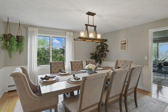 dining space featuring light wood-style flooring, a wainscoted wall, baseboard heating, a chandelier, and a decorative wall