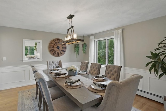 dining area featuring a baseboard radiator, a wainscoted wall, light wood-style flooring, and a chandelier