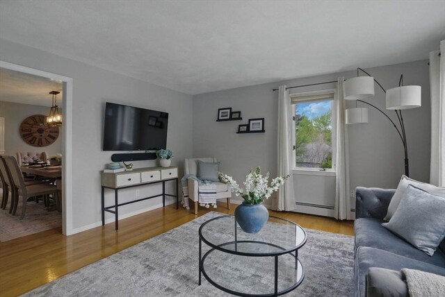 living room featuring wood finished floors, a chandelier, and a baseboard heating unit