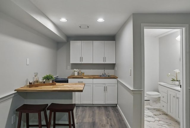 kitchen featuring wood counters, a sink, white cabinets, a kitchen bar, and recessed lighting