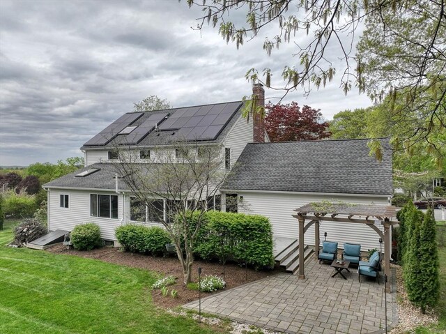 rear view of house with a pergola, a patio, roof mounted solar panels, a lawn, and a shingled roof