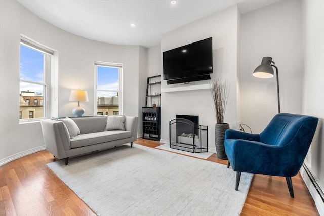 living area with a baseboard heating unit, wood finished floors, baseboards, recessed lighting, and a fireplace