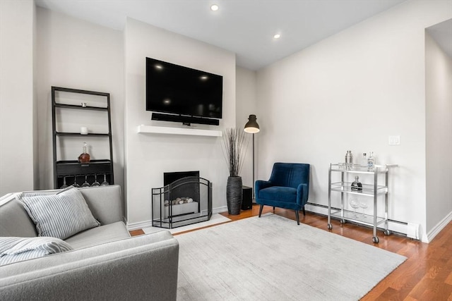 living room with baseboard heating, wood finished floors, baseboards, a fireplace, and recessed lighting