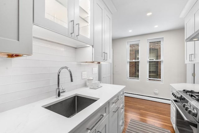 kitchen with a sink, a baseboard heating unit, decorative backsplash, white cabinetry, and glass insert cabinets