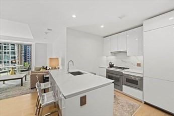 kitchen with sink, a center island with sink, white cabinets, a kitchen bar, and stainless steel oven