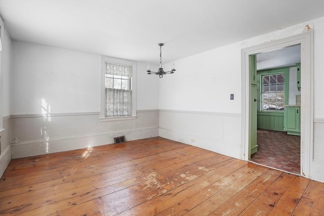 empty room with hardwood / wood-style flooring, visible vents, an inviting chandelier, and wainscoting