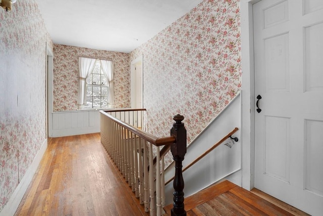 hall featuring wood-type flooring, a wainscoted wall, an upstairs landing, and wallpapered walls