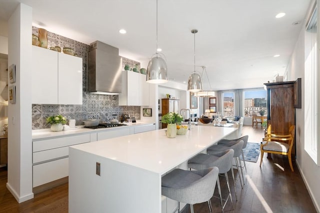 kitchen with tasteful backsplash, a kitchen island, wall chimney range hood, gas stovetop, and a kitchen bar