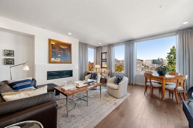 living room featuring recessed lighting, wood-type flooring, a city view, and a glass covered fireplace