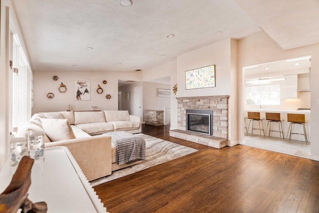 living room featuring lofted ceiling, a healthy amount of sunlight, hardwood / wood-style flooring, and a stone fireplace