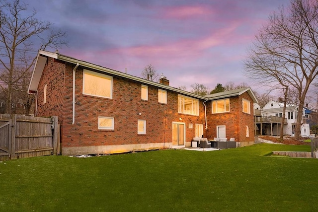 back house at dusk featuring a patio area, a lawn, and outdoor lounge area