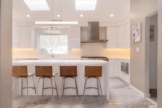 kitchen featuring white cabinetry, a center island, wall chimney exhaust hood, stove, and a breakfast bar