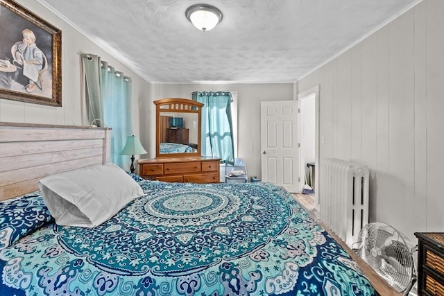 bedroom featuring a textured ceiling, radiator heating unit, wood finished floors, and crown molding