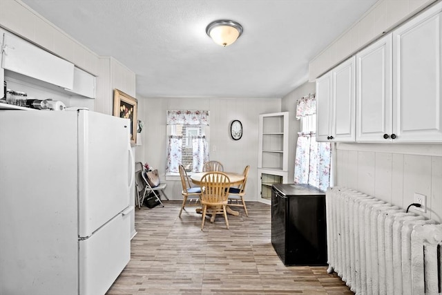 kitchen featuring radiator heating unit, light wood-type flooring, freestanding refrigerator, and white cabinetry