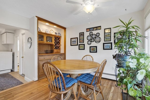 dining space featuring baseboards, light wood-type flooring, a ceiling fan, and a baseboard radiator