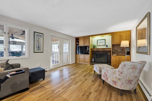 living area featuring a baseboard heating unit, light wood-style floors, a fireplace, and french doors