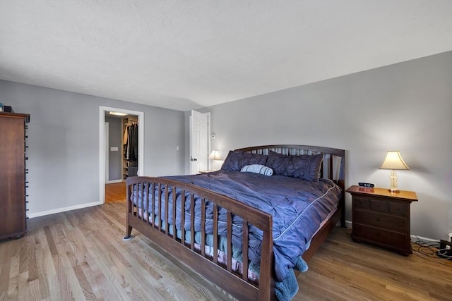 bedroom featuring a spacious closet, baseboards, and wood finished floors