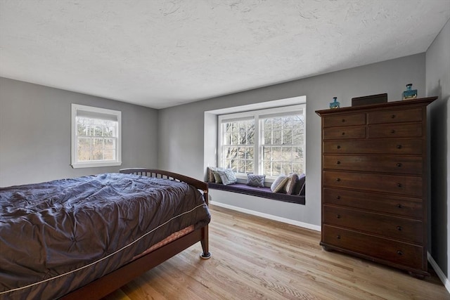 bedroom featuring baseboards, a textured ceiling, and light wood finished floors