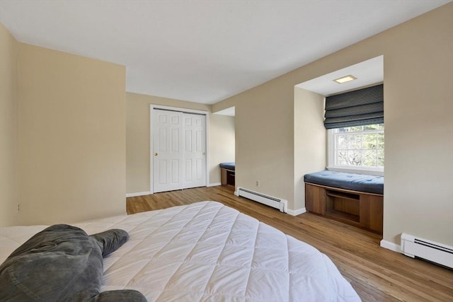 bedroom with a closet, baseboards, baseboard heating, and wood finished floors