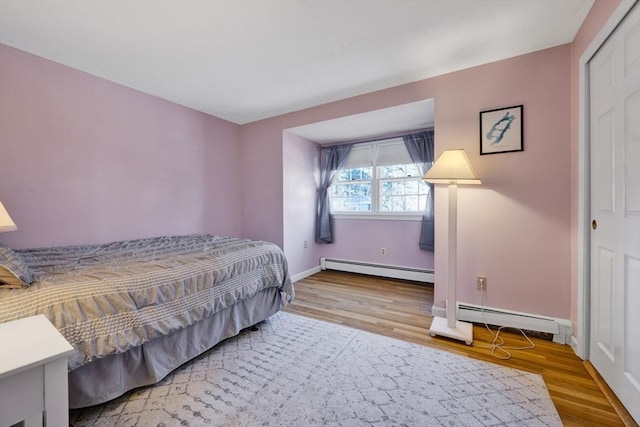 bedroom featuring a baseboard heating unit, wood finished floors, and baseboards