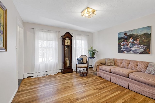 living area with baseboard heating, a textured ceiling, baseboards, and light wood-style floors