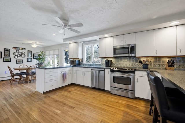 kitchen with a ceiling fan, light wood-type flooring, a peninsula, appliances with stainless steel finishes, and tasteful backsplash